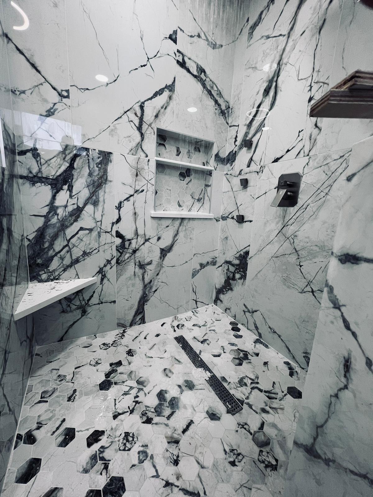 Luxury shower with white and black marble walls, built-in shelves, and a hexagonal marble tile floor.