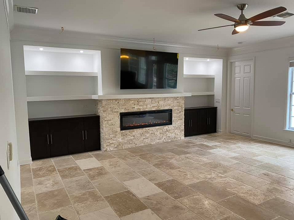 Modern living room with a stone fireplace, built-in shelving, and a mounted flat-screen TV.